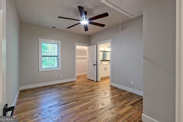 unfurnished bedroom featuring ensuite bathroom, a walk in closet, hardwood / wood-style flooring, ceiling fan, and a closet