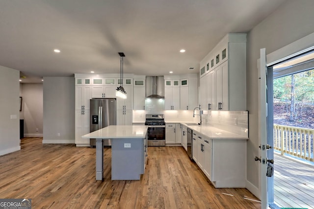 kitchen with pendant lighting, a center island, wall chimney range hood, appliances with stainless steel finishes, and light hardwood / wood-style floors