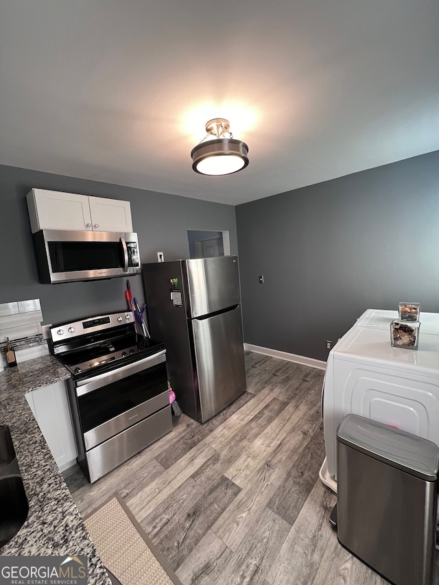 kitchen with white cabinets, light hardwood / wood-style flooring, stainless steel appliances, washer / dryer, and dark stone countertops