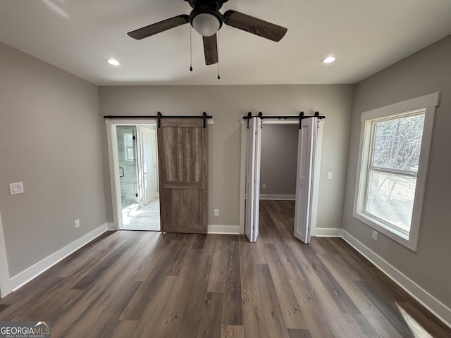 unfurnished bedroom featuring dark hardwood / wood-style floors, ceiling fan, and a barn door