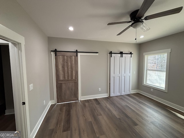 unfurnished bedroom featuring ceiling fan, dark hardwood / wood-style flooring, and a barn door