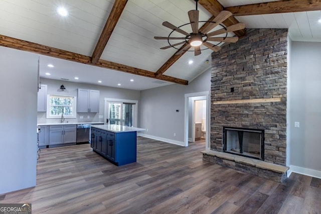 kitchen featuring a kitchen island, a fireplace, dark hardwood / wood-style flooring, stainless steel dishwasher, and beam ceiling