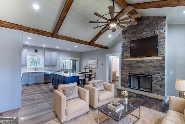 living room with light wood-type flooring, a stone fireplace, and beam ceiling