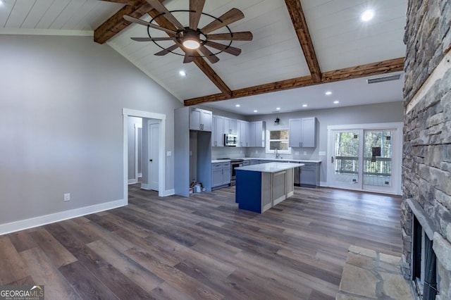 kitchen featuring dark wood-type flooring, beam ceiling, stainless steel appliances, a kitchen island, and a stone fireplace