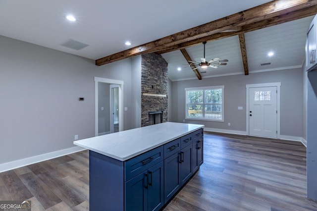 kitchen featuring a stone fireplace, lofted ceiling with beams, dark hardwood / wood-style floors, a kitchen island, and ceiling fan