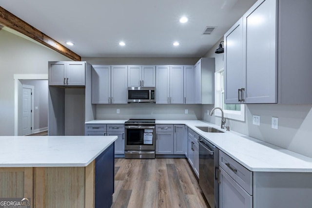 kitchen with gray cabinets, appliances with stainless steel finishes, sink, and hardwood / wood-style flooring