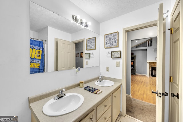 bathroom with wood-type flooring, a stone fireplace, vanity, and a textured ceiling