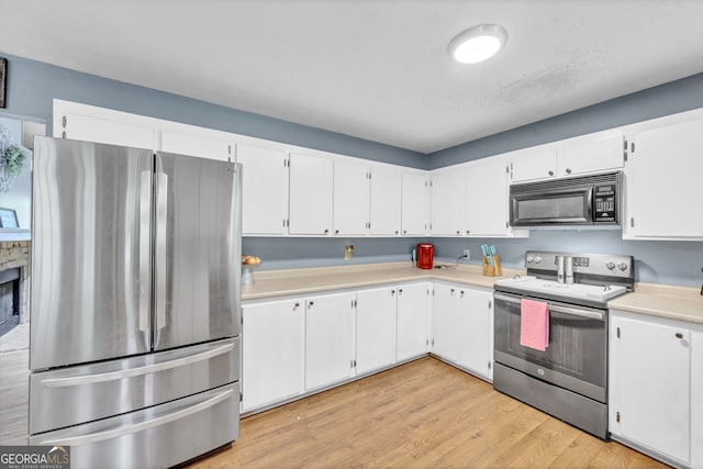 kitchen with a stone fireplace, appliances with stainless steel finishes, light wood-type flooring, and white cabinetry