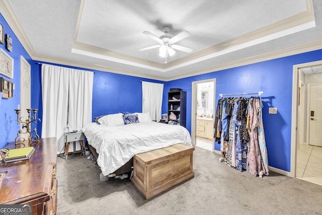 carpeted bedroom featuring ceiling fan, a textured ceiling, a tray ceiling, crown molding, and ensuite bathroom