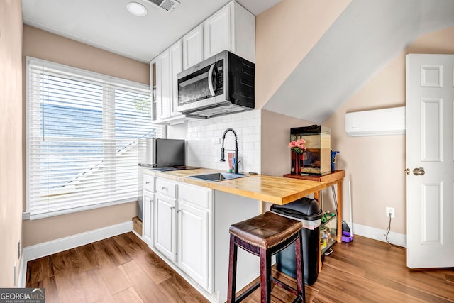 kitchen featuring white cabinets, light hardwood / wood-style flooring, a wall unit AC, and wood counters