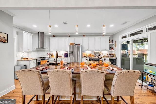 kitchen featuring hanging light fixtures, appliances with stainless steel finishes, wall chimney exhaust hood, and a kitchen island with sink