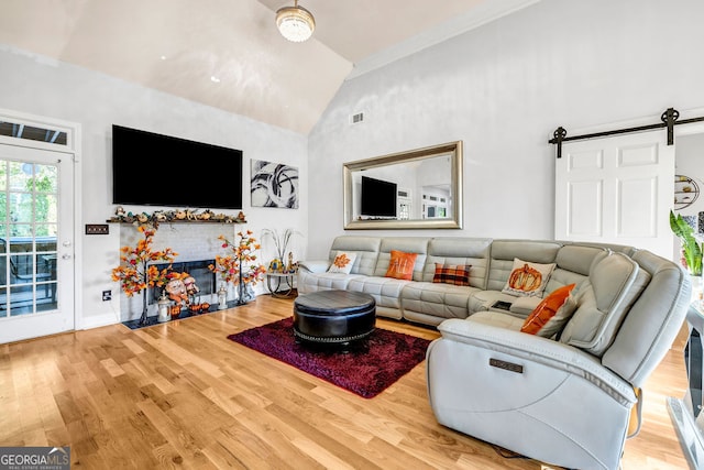 living room with a barn door, ornamental molding, high vaulted ceiling, and hardwood / wood-style flooring