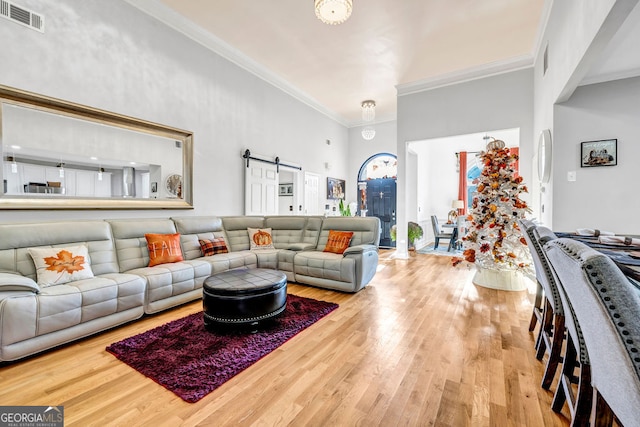 living room with a barn door, ornamental molding, a high ceiling, and hardwood / wood-style floors