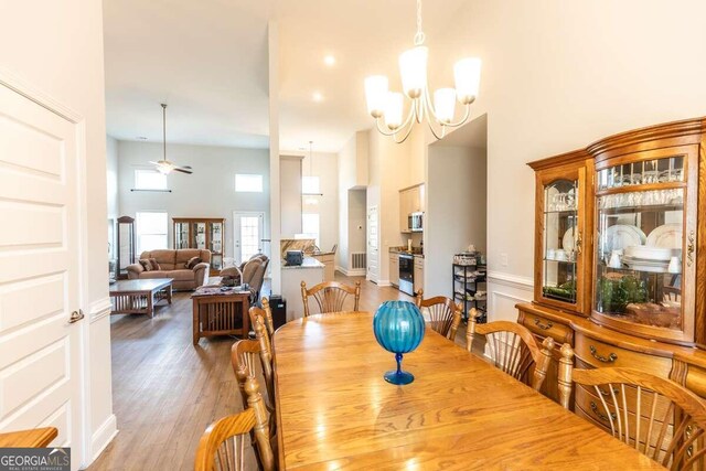 dining room featuring ceiling fan with notable chandelier, a high ceiling, and hardwood / wood-style flooring