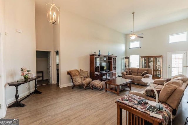 living room featuring ceiling fan with notable chandelier, wood-type flooring, and a towering ceiling