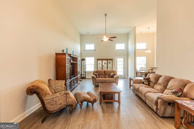 living room with ceiling fan with notable chandelier, light wood-type flooring, and a high ceiling