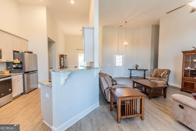 kitchen featuring pendant lighting, light wood-type flooring, a kitchen bar, stainless steel appliances, and light stone countertops