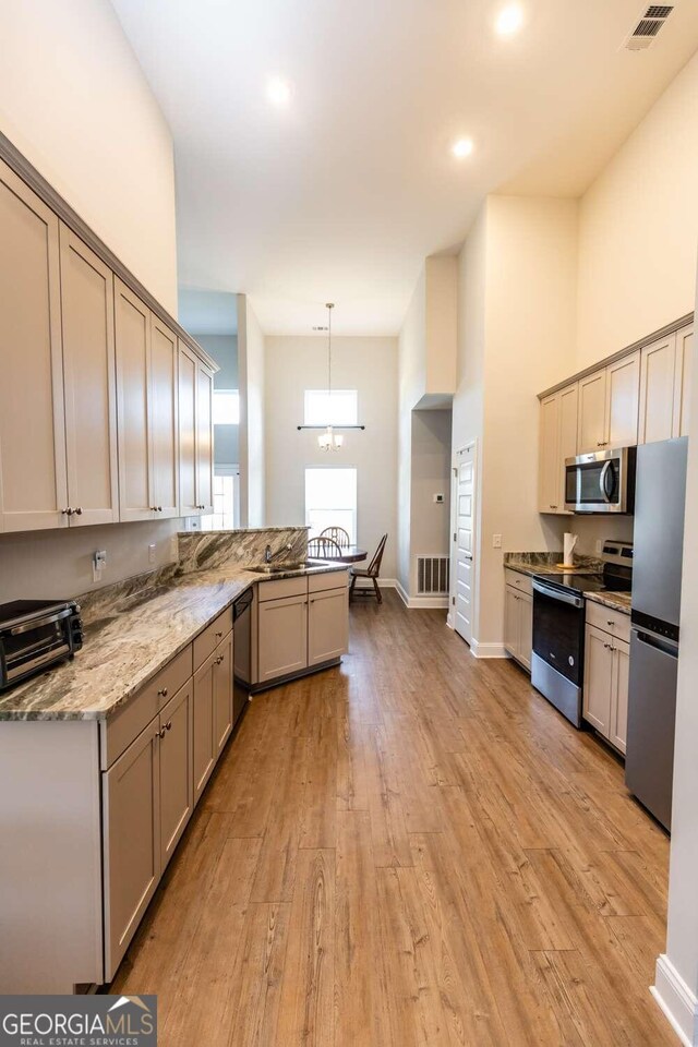 kitchen with decorative light fixtures, stainless steel appliances, light wood-type flooring, and kitchen peninsula