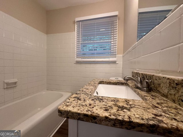 bathroom with tile walls, a tub to relax in, and vanity