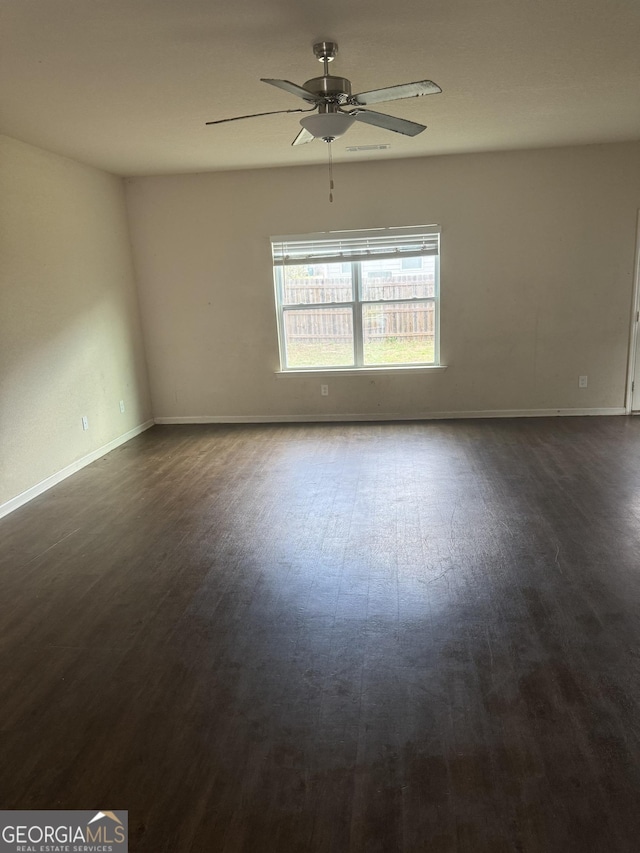 unfurnished room featuring dark wood-style flooring, a ceiling fan, and baseboards