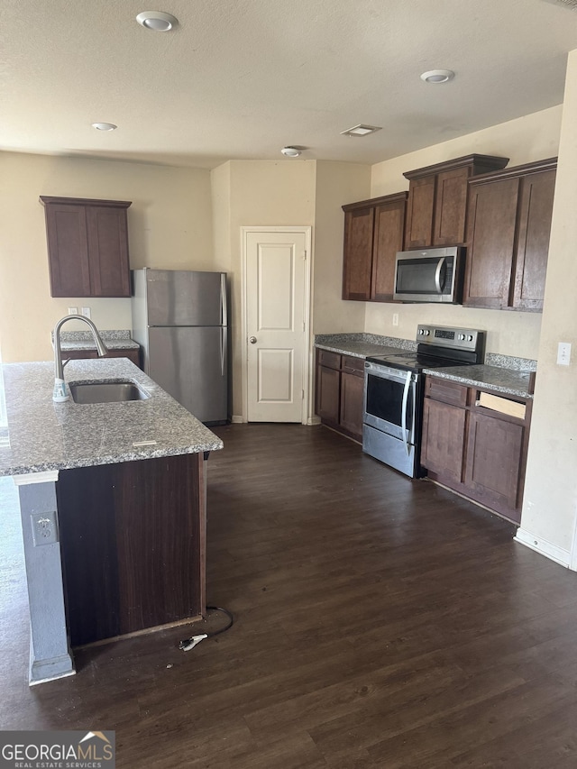 kitchen with dark wood-style floors, stone countertops, stainless steel appliances, and a sink