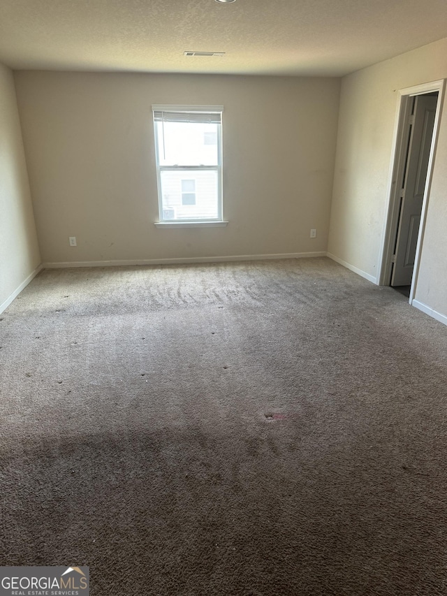 carpeted empty room with baseboards, visible vents, and a textured ceiling