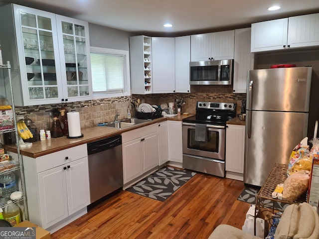 kitchen featuring appliances with stainless steel finishes, light wood-type flooring, tasteful backsplash, sink, and white cabinets