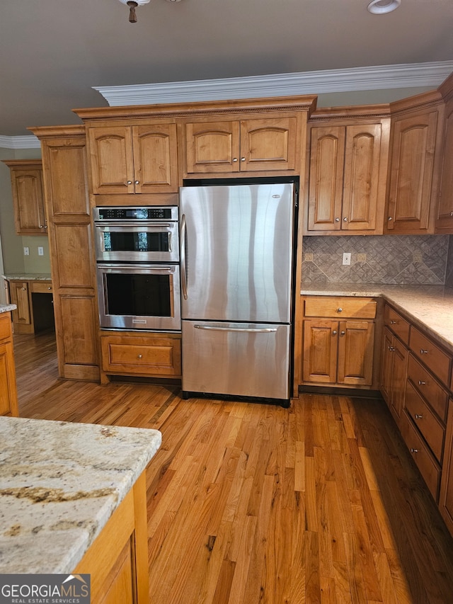 kitchen with appliances with stainless steel finishes, light hardwood / wood-style floors, tasteful backsplash, light stone countertops, and ornamental molding