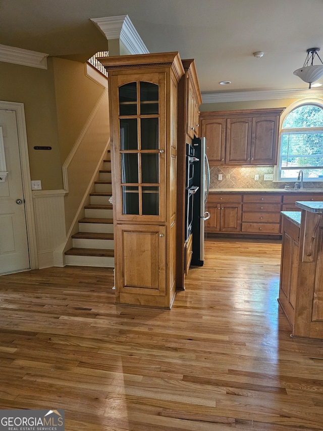 kitchen featuring appliances with stainless steel finishes, light hardwood / wood-style floors, backsplash, crown molding, and sink