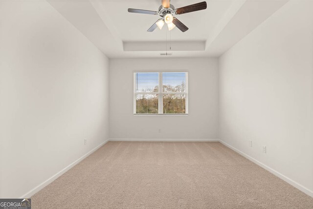 empty room with light carpet, a tray ceiling, and ceiling fan