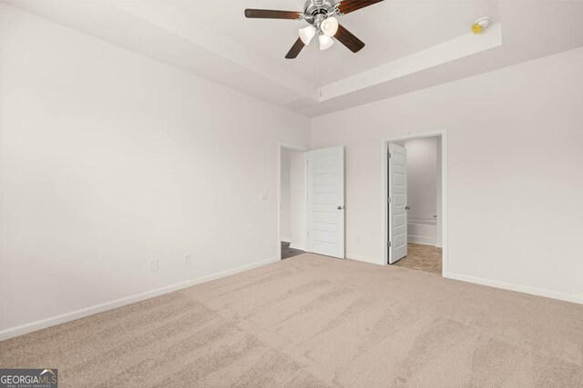 unfurnished bedroom featuring a tray ceiling, light carpet, ceiling fan, and ensuite bathroom