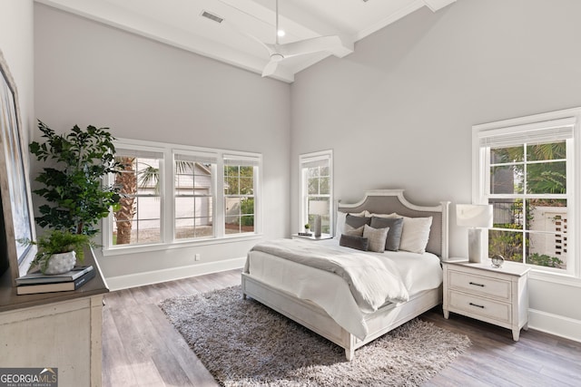 bedroom with high vaulted ceiling, beam ceiling, hardwood / wood-style floors, and multiple windows