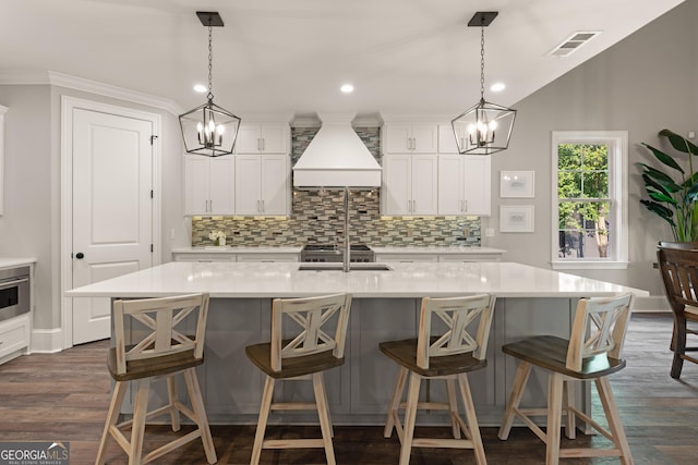 kitchen featuring decorative light fixtures, a kitchen bar, a large island, dark wood-type flooring, and custom range hood