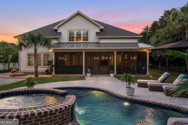 back house at dusk with a pool with hot tub, a sunroom, a patio, and pool water feature