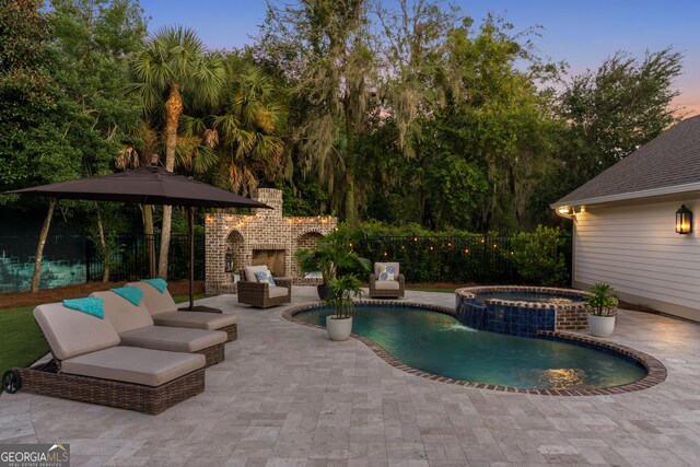 pool at dusk with an in ground hot tub, an outdoor living space with a fireplace, and a patio area