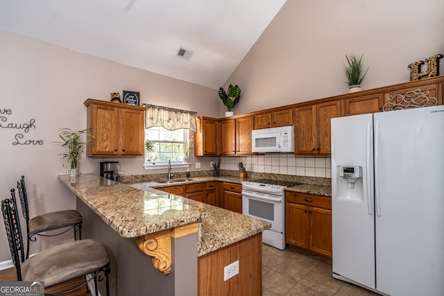 kitchen featuring light stone counters, white appliances, a kitchen bar, and kitchen peninsula