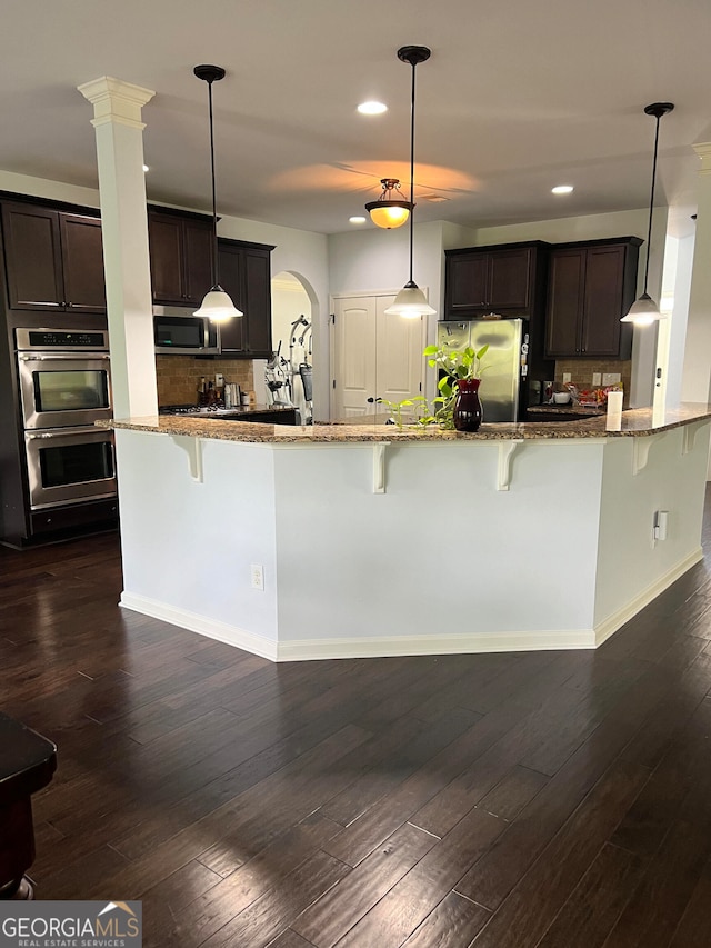 kitchen featuring appliances with stainless steel finishes, dark hardwood / wood-style flooring, a kitchen bar, and hanging light fixtures