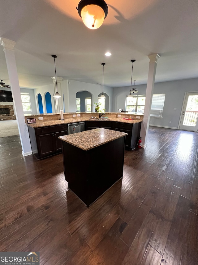 kitchen featuring a kitchen island, dark hardwood / wood-style flooring, hanging light fixtures, stainless steel dishwasher, and light stone counters