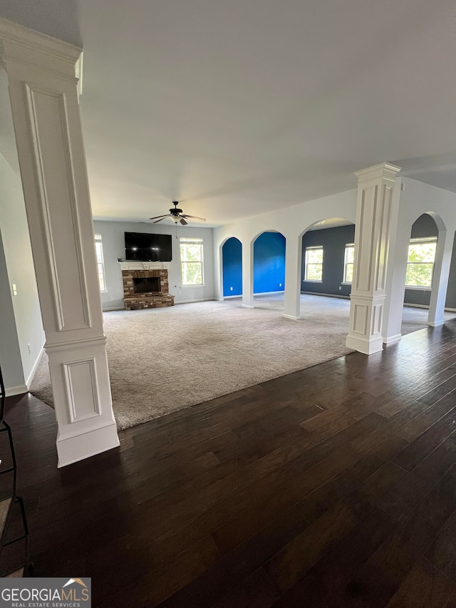 unfurnished living room featuring dark wood-type flooring, ornate columns, a fireplace, and ceiling fan