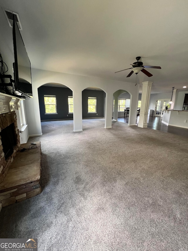 unfurnished living room featuring ceiling fan, a stone fireplace, decorative columns, and carpet floors