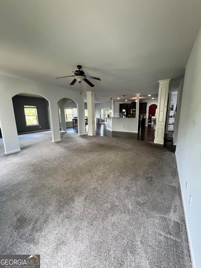 unfurnished living room featuring dark colored carpet, ornate columns, and ceiling fan