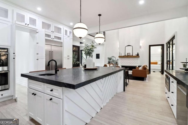 kitchen with white cabinets, sink, a kitchen island with sink, built in appliances, and light wood-type flooring