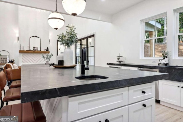 kitchen with light hardwood / wood-style floors, dark stone counters, decorative light fixtures, white cabinets, and a center island