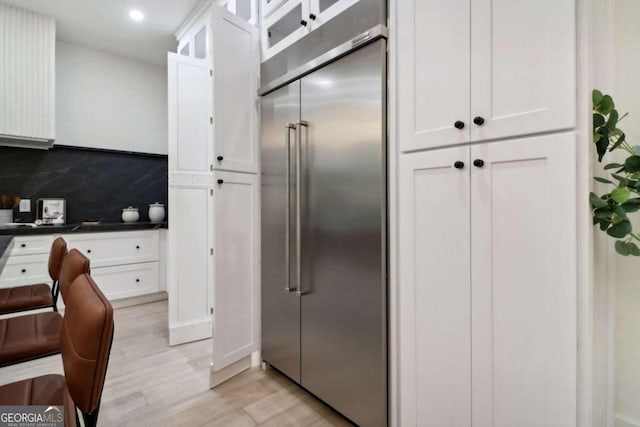 kitchen featuring tasteful backsplash, stainless steel built in fridge, white cabinetry, and light wood-type flooring