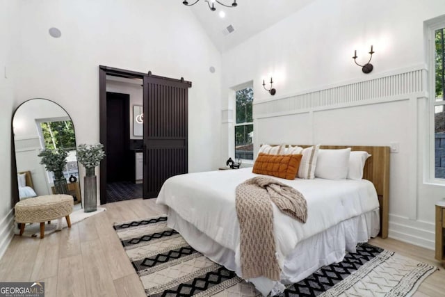 bedroom with high vaulted ceiling, a barn door, and light hardwood / wood-style flooring