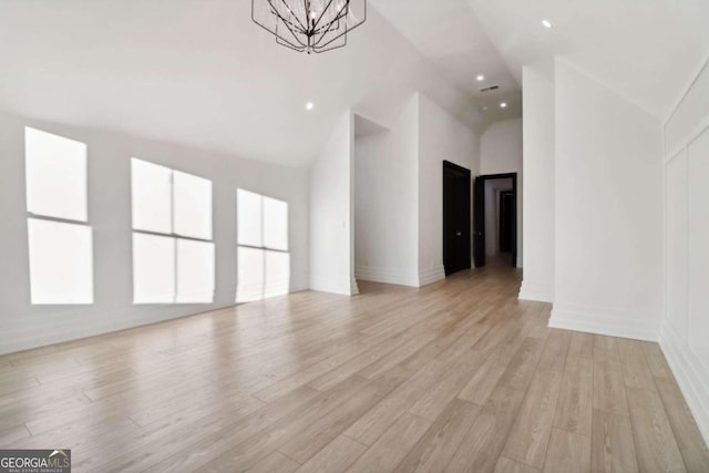 unfurnished living room with light hardwood / wood-style floors, high vaulted ceiling, and a notable chandelier