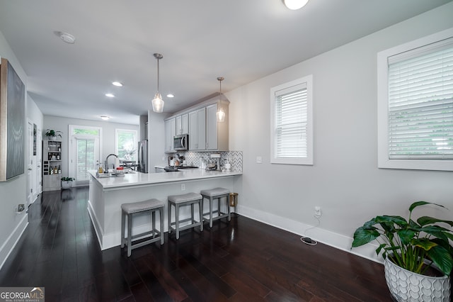 kitchen with pendant lighting, kitchen peninsula, stainless steel appliances, dark hardwood / wood-style floors, and a kitchen breakfast bar