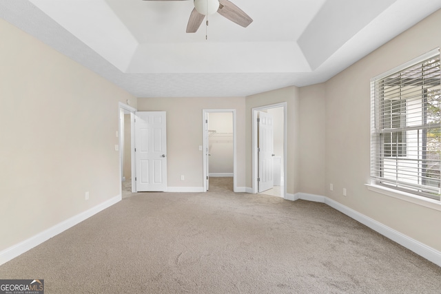 unfurnished bedroom with a spacious closet, carpet, ceiling fan, and a tray ceiling