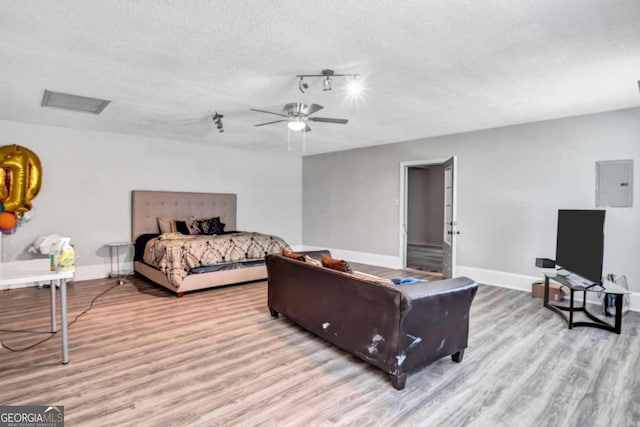 bedroom featuring ceiling fan, a textured ceiling, light wood-type flooring, and electric panel