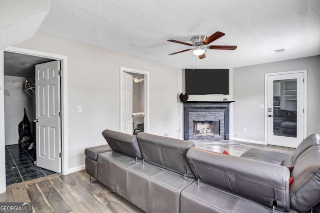 living room featuring wood-type flooring, a textured ceiling, a fireplace, and ceiling fan